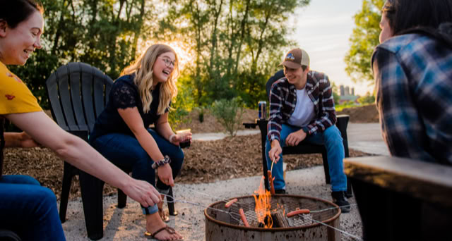 People roasting hot dogs over a fire, looking happy.
