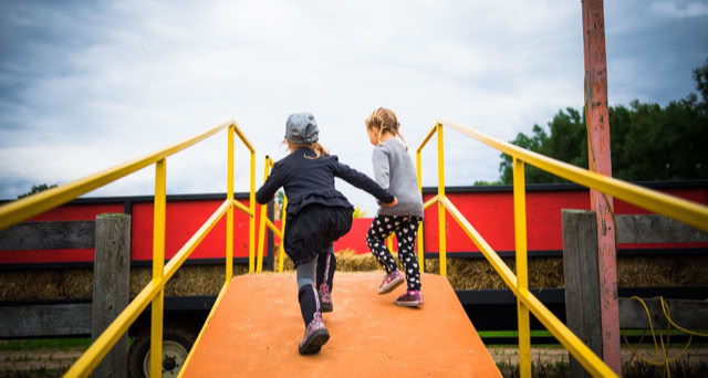 Two children running up a ramp with railings into a hay wagon.