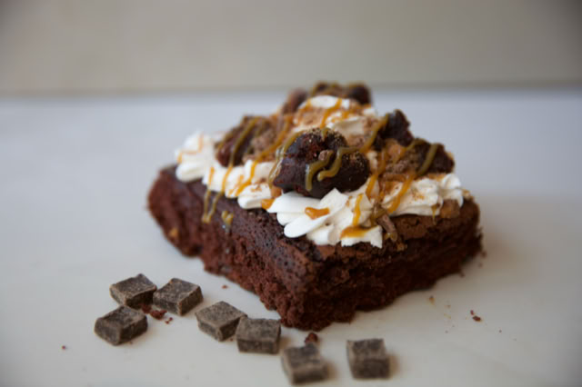 Piece of chocolate cake topped with whipped cream, caramel drizzle, and chocolates.